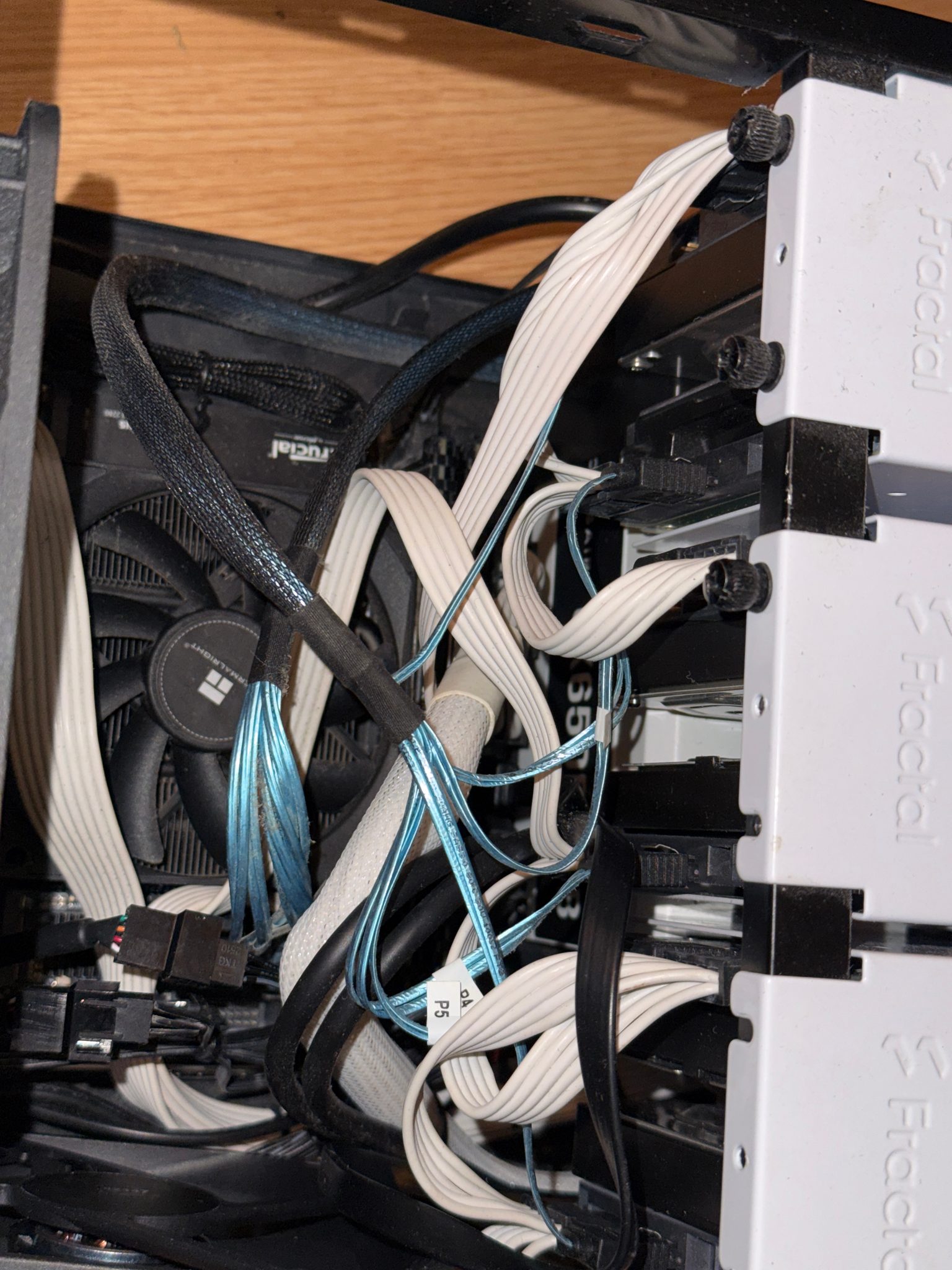 Close-up of Fractal drive trays with white-sleeved power cables, labelled blue SATA cables, and a Thermalright CPU cooler