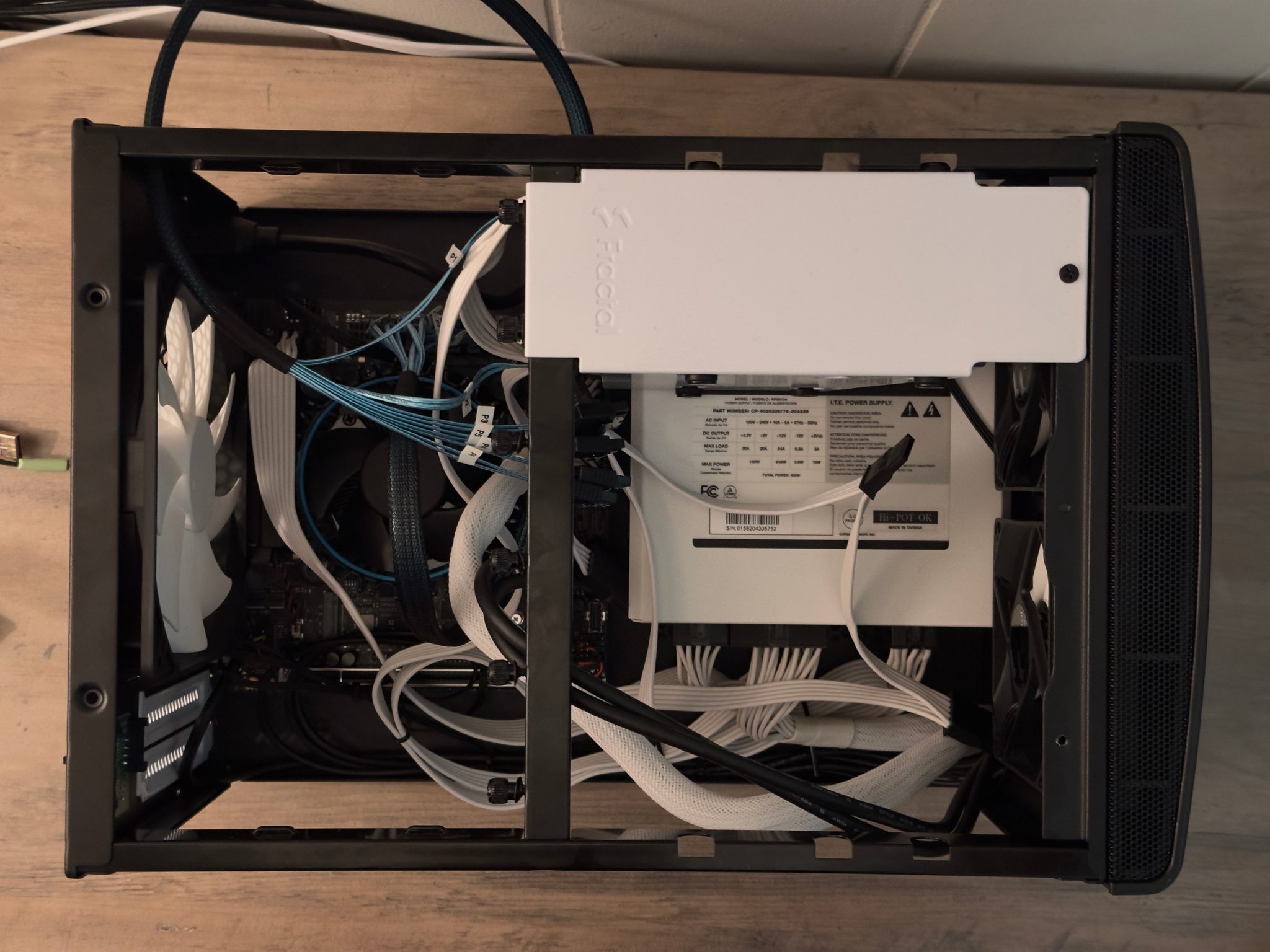 Top-down view of the Fractal case, with a white 500W power supply, labelled cables, and a white exhaust fan