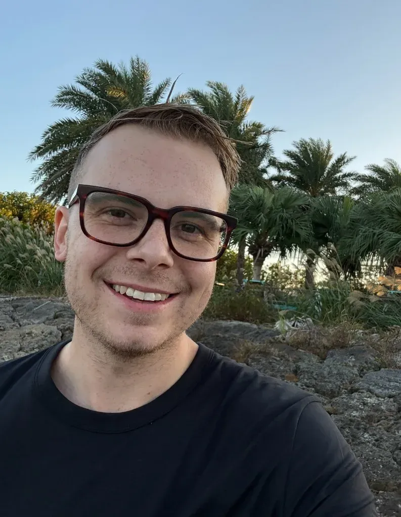 Sean Courtney smiling outdoors in glasses and a black t-shirt